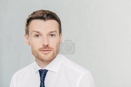 Photo for Attractive male freelancer with confident serious expression, works distantly, dressed in elegant white shirt with tie, isolated over white studio wall. People, facial expressions and work concept - Royalty Free Image