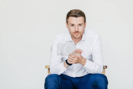Photo for Indoor portrait of handsome self confident businessman in white shirt and black trousers, looks with serious expression, ready to have business meeting with colleagues, isolated over white studio - Royalty Free Image