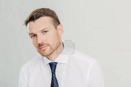 Photo for Confident male looks seriously at camera, has dark eyes and stubble, dressed in elegant white shirt with tie, isolated over white background. Man director thinks about how reach success in life - Royalty Free Image
