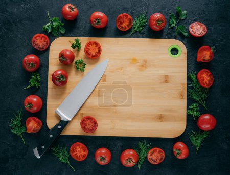 Photo for Horizontal top view of red tomatoes lying around wooden chopping board. Green parsley and dill. Knife near. Vegan table. Food concept - Royalty Free Image