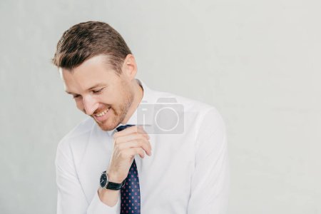 Photo for Positive unshaven man looks happily down, dressed in elegant clothes, stands against white background, isolated over white background with free space for advertising content. Happy male boss - Royalty Free Image
