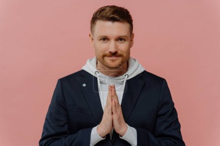 Photo for Serious bearded adult man keeps palms pressed together prays for something looks directly at camera believes in something good happen poses against pink background. Handsome guy makes request - Royalty Free Image