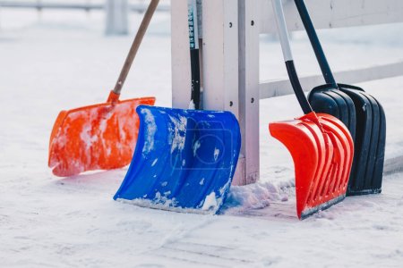 Outdoor shot of colourful shovels against snow background during winter. Cleaning roads concept. Four spades for cleaning territory after heavy snowfall