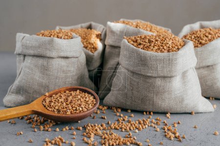 Photo for Horizontal shot of roasted buckwheat in sacks and spoon. Gluten free grains. Harvested uncooked cereals. Natural vegan food concept - Royalty Free Image