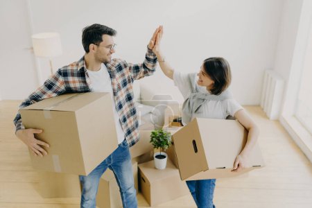 Photo for New home. Happy woman and man celebrate moving to new apartment, pose in empty room with cardboard boxes and couch in background, give each other high five. People, home, real estate concept - Royalty Free Image
