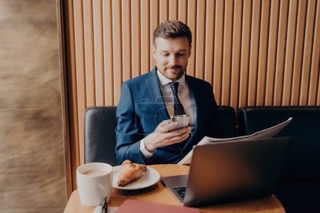 Photo for Confident businessman in formal attire juggles coffee, smartphone, laptop, and newspaper at coffee shop. - Royalty Free Image
