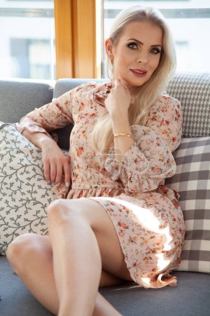 Téléchargez les photos : Portrait de jolie jeune blonde jolie femme en robe de fleurs assis sur l'entraîneur - en image libre de droit