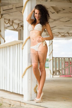Téléchargez les photos : Jeune adulte jolie jolie femme brune mince dans un maillot de bain blanc sur une terrasse ensoleillée - en image libre de droit