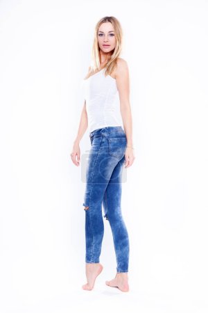 Téléchargez les photos : Figure séduisante sexy et sensualité jeune femme blonde adulte en jeans bleu pantalon et pieds recherchés isolés sur fond blanc - en image libre de droit