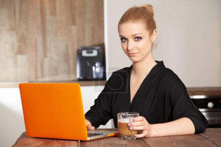 Foto de Retrato de una atractiva joven adulta bastante rubia estudiante trabajando en el ordenador naranja - Imagen libre de derechos