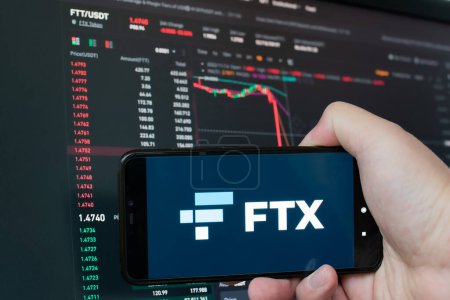 Hombre sosteniendo el teléfono con logo FTX. Caída global del gráfico criptomoneda - FTT token cayó en el gráfico de intercambios criptomoneda en la pantalla de la aplicación. FTX bancarrota de cambio y la depreciación del colapso de ficha