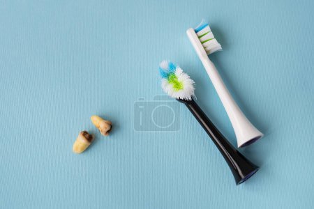 Foto de Un moderno cepillo de dientes eléctrico sobre un fondo azul junto a las muelas del juicio extraídas afectadas por la caries. Operación de extracción dental. Concepto de higiene para el cuidado diario. Cepillo de dientes viejo y nuevo - Imagen libre de derechos