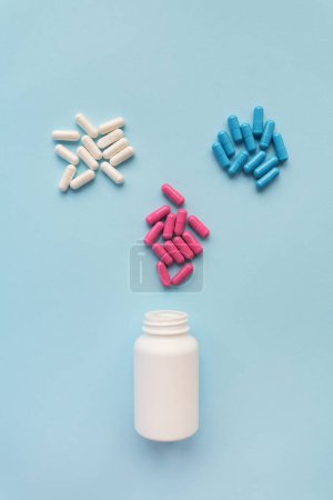 Foto de Varias píldoras de cápsulas brillantes multicolores que vuelan desde una botella de plástico abierta aislada sobre un fondo azul. Concepto de medicina basada en la evidencia y atención sanitaria - Imagen libre de derechos