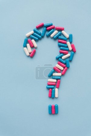 Question mark consisting of three multi-colored vitamins on a blue background. Health problems and treatment. The concept of evidence-based medicine