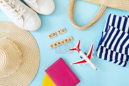 Téléchargez les photos : Aller sur une inscription de voyage sur un fond bleu avec un passeport, un avion jouet, baskets, un sac, un chapeau de paille - en image libre de droit