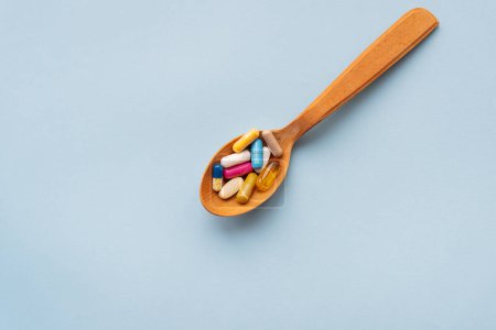 Foto de Varias pastillas brillantes sobre un fondo azul yacen en una cuchara de madera. Concepto de salud y medicina basada en la evidencia, primer plano - Imagen libre de derechos
