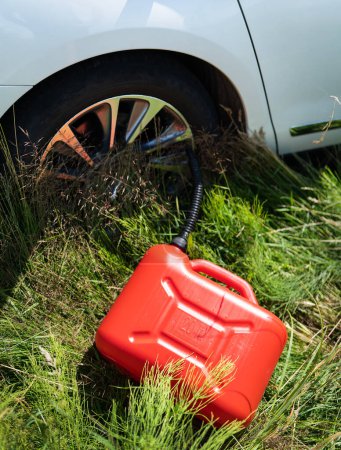 Foto de Bote de plástico rojo entre la hierba verde cerca del coche blanco. Problemas en la carretera con el combustible para el coche - Imagen libre de derechos