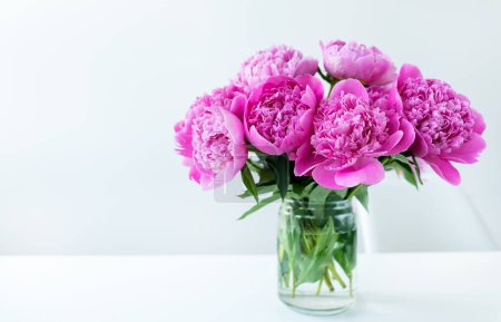 Photo for Festive background. Still life, birthday or wedding concept. A bouquet of pink peonies on a white table stands in a transparent vase - Royalty Free Image