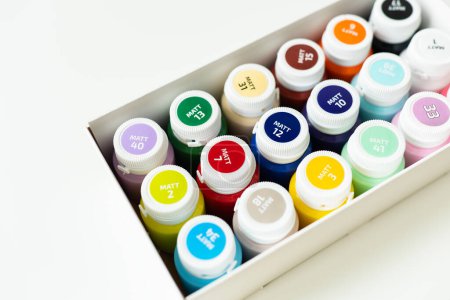 A box of colorful paint bottles, neatly arranged, showcasing vibrant hues. Labels on caps indicate paint colors
