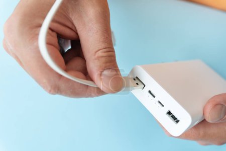Nahaufnahme einer Hand, die ein USB-Kabel mit einer weißen Strombank auf blauem Hintergrund verbindet