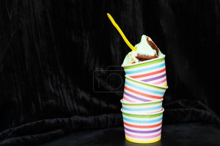 Bunt gestreifte Tasse mit cremigem Schokoladeneis und gelbem Löffel auf dunkel strukturiertem Hintergrund