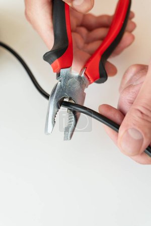 Photo for Close-up of hands using red and black pliers to cut a black cable on a white background - Royalty Free Image