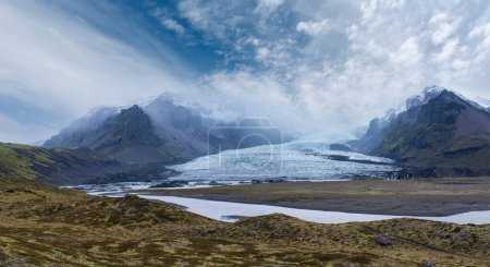 Photo for Glacier tongue slides from the Vatnajokull icecap or Vatna Glacier near subglacial Oraefajokull volcano, Iceland. Glacial lagoon with ice blocks and surrounding mountains. - Royalty Free Image
