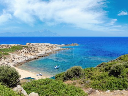Téléchargez les photos : Bateau près d'une tente de camping simple sur la côte de mer pierreuse d'été avec vue sur le mont Atthos à l'extrême (Halkidiki, Sithonie, Grèce). - en image libre de droit