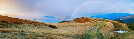 Photo for Dusk Carpathian Mountains (Ukraine) autumn landscape with country dirty road and rainbow in the sky. - Royalty Free Image