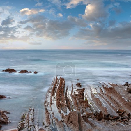Photo for Twilight ocean coast with ribbed stratiform rock formations. (Atlantic Ocean, Spain). - Royalty Free Image