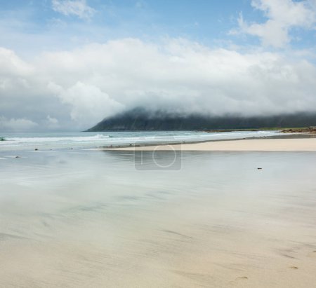 Téléchargez les photos : Vue sur la plage brumeuse et nuageuse avec des reflets de ciel dans l'eau de vague couverte de sable blanc (Ramberg, Lofoten, Norvège
). - en image libre de droit