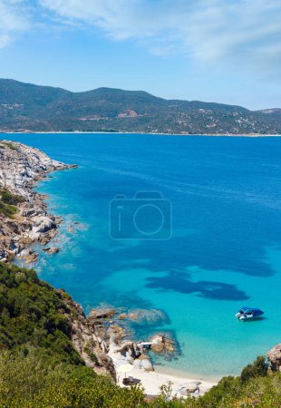 Sommer-Meereslandschaft mit Boot in aquamarinklarem Wasser und Sandstrand an der felsigen Küste. Blick vom Ufer (Sithonia, Chalkidiki, Griechenland)).