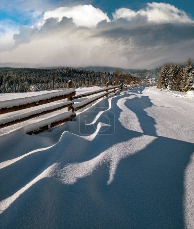 Photo for Picturesque waved shadows on snow from wood fence. Alpine mountain winter hamlet outskirts, snowy path, fir forest. High resolution image with great depth of field. - Royalty Free Image