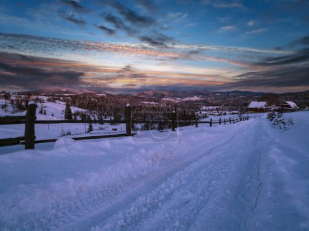 Photo for Night countryside road, hoases, hills, groves and farmlands in winter remote alpine mountain village. Ukraine, Voronenko, Moon above village. - Royalty Free Image