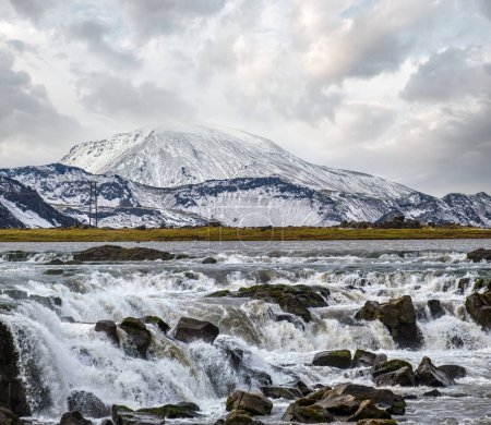 Photo for Season changing in southern Highlands of Iceland. Picturesque waterfal Tungnaarfellsfoss panoramic autumn view.  Landmannalaugar mountains under snow cover in far. - Royalty Free Image
