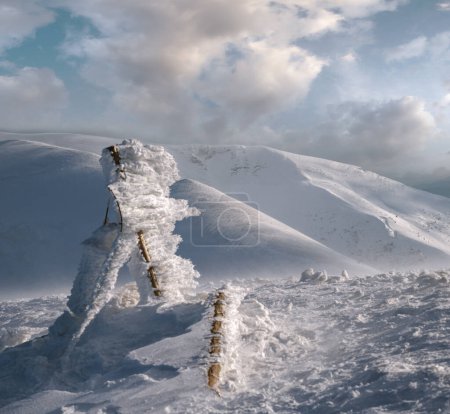 Foto de Señalización cubierta de nieve y montañas de invierno en la última noche la luz del sol. Magnífico atardecer ventoso en la parte superior de la pintoresca estación de esquí alpino. Concéntrate en montañas lejanas. - Imagen libre de derechos
