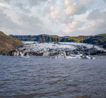 Foto de Glaciar Solheimajokull en el sur de Islandia. La lengua de este glaciar se desliza desde el volcán Katla. Hermosa laguna glacial con bloques de hielo y montañas circundantes. Personas irreconocibles. - Imagen libre de derechos
