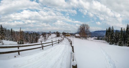Photo for Secondary countryside alpine road in remote mountain village, snow drifts and wood fence on wayside - Royalty Free Image