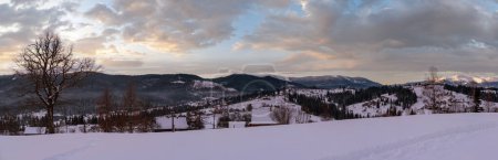 Téléchargez les photos : Petit village alpin et montagnes enneigées d'hiver au premier lever du soleil autour, Voronenko, Carpates, Ukraine. Trace sur un sentier fraîchement foulé à travers des dérives de neige. - en image libre de droit
