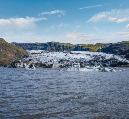 Téléchargez les photos : Glacier Solheimajokull dans le sud de l'Islande. La langue de ce glacier glisse du volcan Katla. Beau lagon lacustre glaciaire avec blocs de glace et montagnes environnantes. Des gens méconnaissables. - en image libre de droit