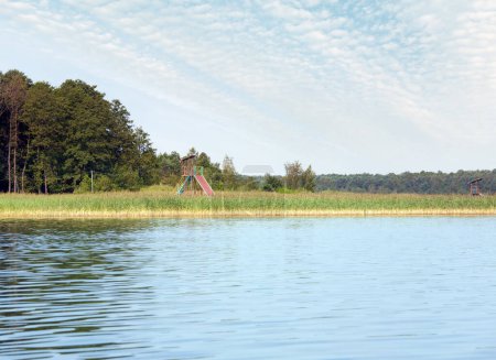 Téléchargez les photos : Vue sur le lac rushy d'été avec petit bosquet sur la rive opposée et pont d'observation - en image libre de droit