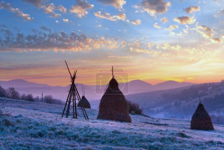 Photo for First autumn frosts on pasture with haystacks and sunrise in the mountains village - Royalty Free Image