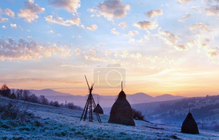 Téléchargez les photos : Premières gelées d'automne sur pâturage avec des meules de foin et lever de soleil majestueux dans le village de montagne - en image libre de droit
