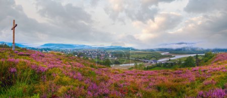 Summer misty morning country foothills panorama with heather flowers and wooden cross (Lviv Oblast, Ukraine) .