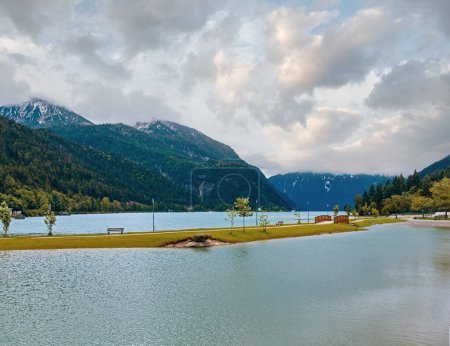 Achensee Sommerlandschaft mit Holzbrücke und Wolkenspiegelung auf der Wasseroberfläche (Österreich).