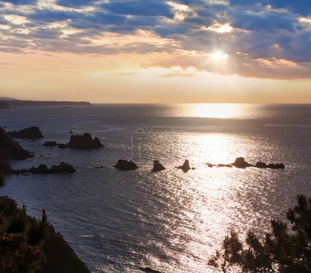 Foto de Paisaje de la costa del océano Atlántico nocturno con islotes afilados cerca de la playa de Gueirua y reflejo del sol en la superficie del agua, Asturias, España
. - Imagen libre de derechos