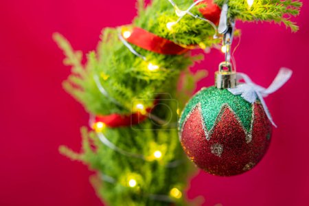 Photo for Close up of a cute but sad christmas tree with led lights and one single ornament on a red background - Royalty Free Image