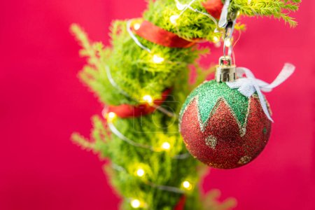 Foto de Primer plano de un árbol de Navidad lindo pero triste con luces led y un solo adorno sobre un fondo rojo - Imagen libre de derechos