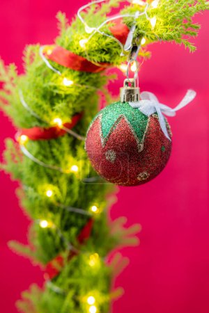 Téléchargez les photos : Gros plan d'un arbre de Noël mignon mais triste avec des lumières LED et un seul ornement sur un fond rouge - en image libre de droit
