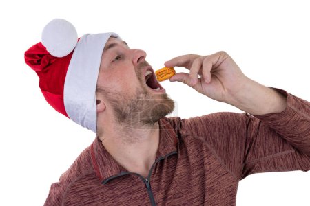 Photo for Portrait of a caucasian male wearing a santa hat eating a French macaroni isolated on a white background - Royalty Free Image